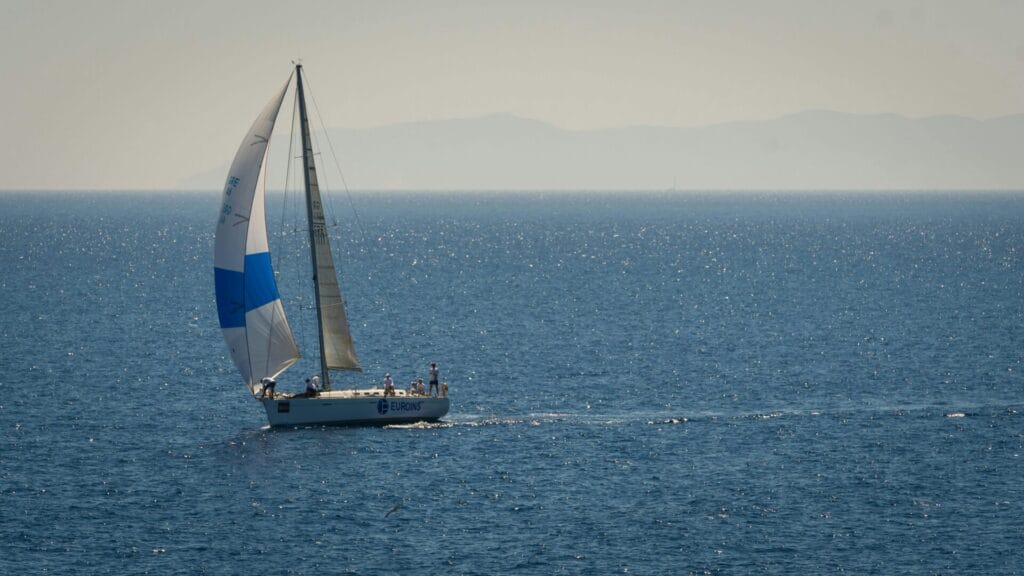 A sailboat glides across a sparkling blue ocean under a clear summer sky, epitomizing leisure and travel.