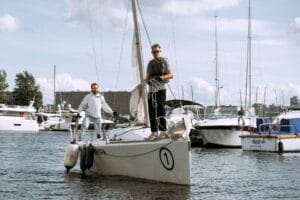 Two adults on a yacht preparing to sail at a marina on a sunny day.